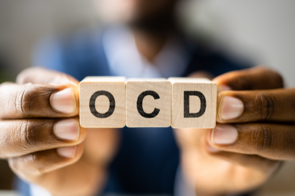 Alt Text Person holding three wooden blocks spelling out OCD, representing obsessive-compulsive disorder and the hidden mental compulsions that many people silently experience.