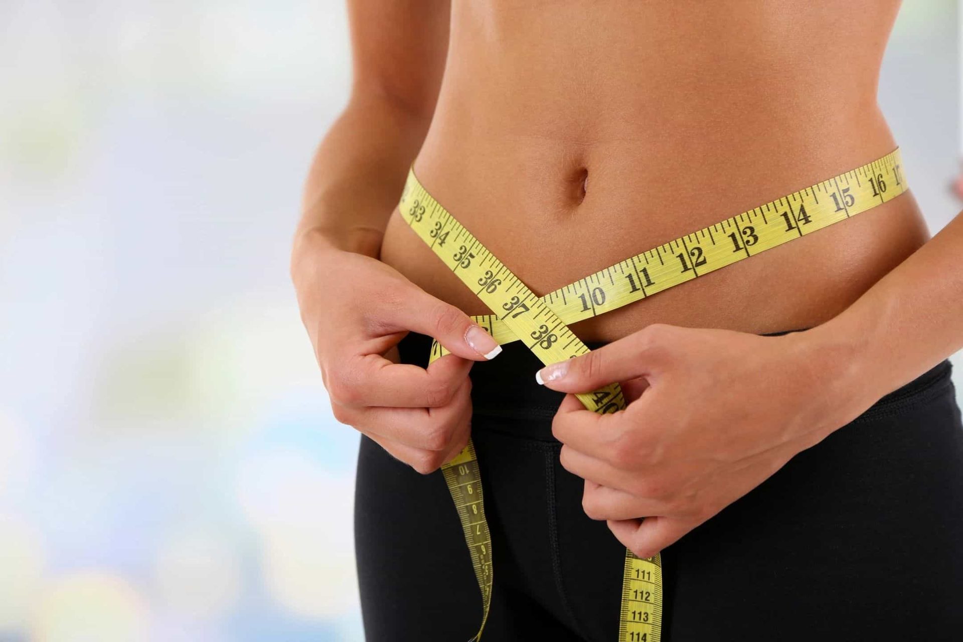 Slim woman measuring her waist with yellow tape, wellness and weight management concept.