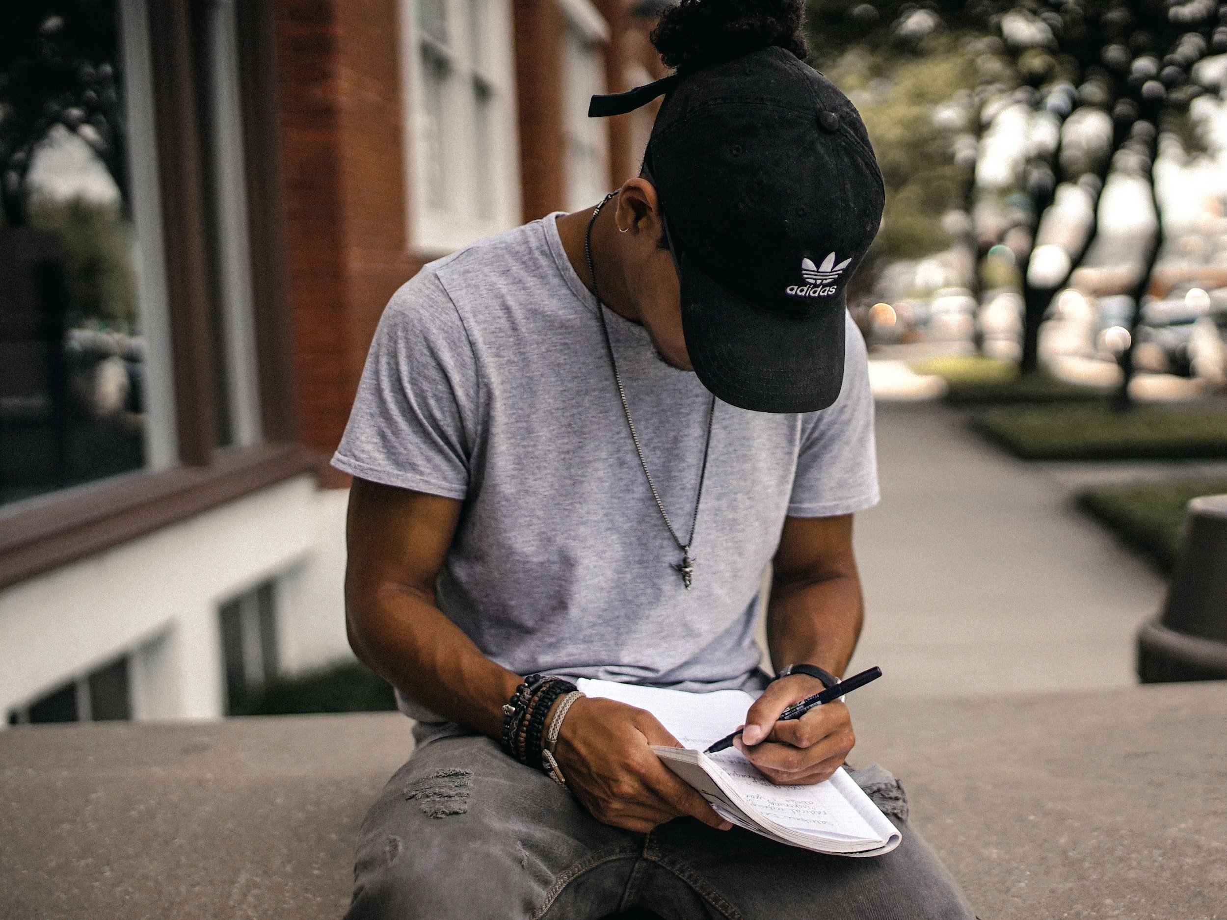 Person wearing a cap writing in a notebook outdoors.