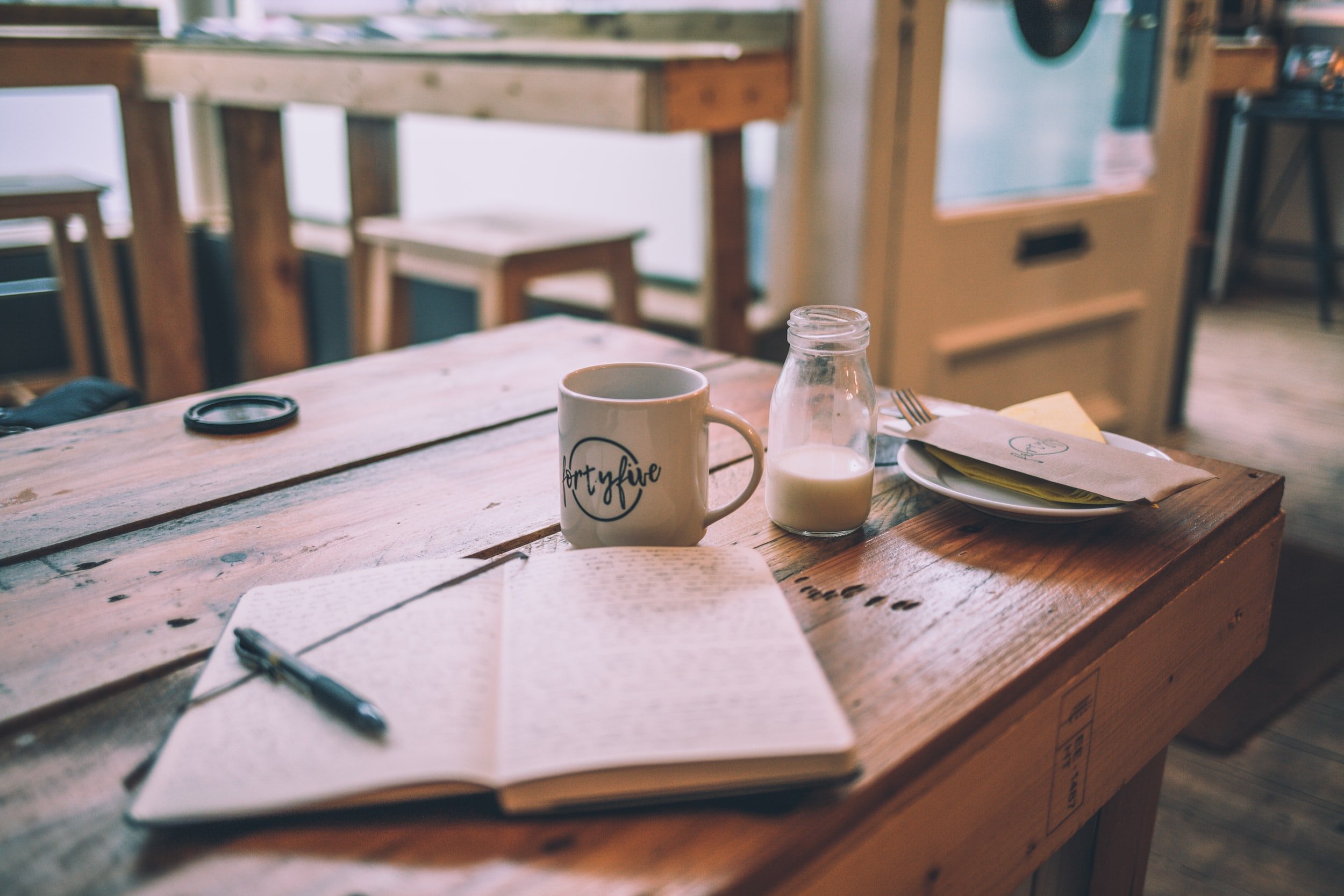 Open notebook, coffee mug, and milk on wooden table.