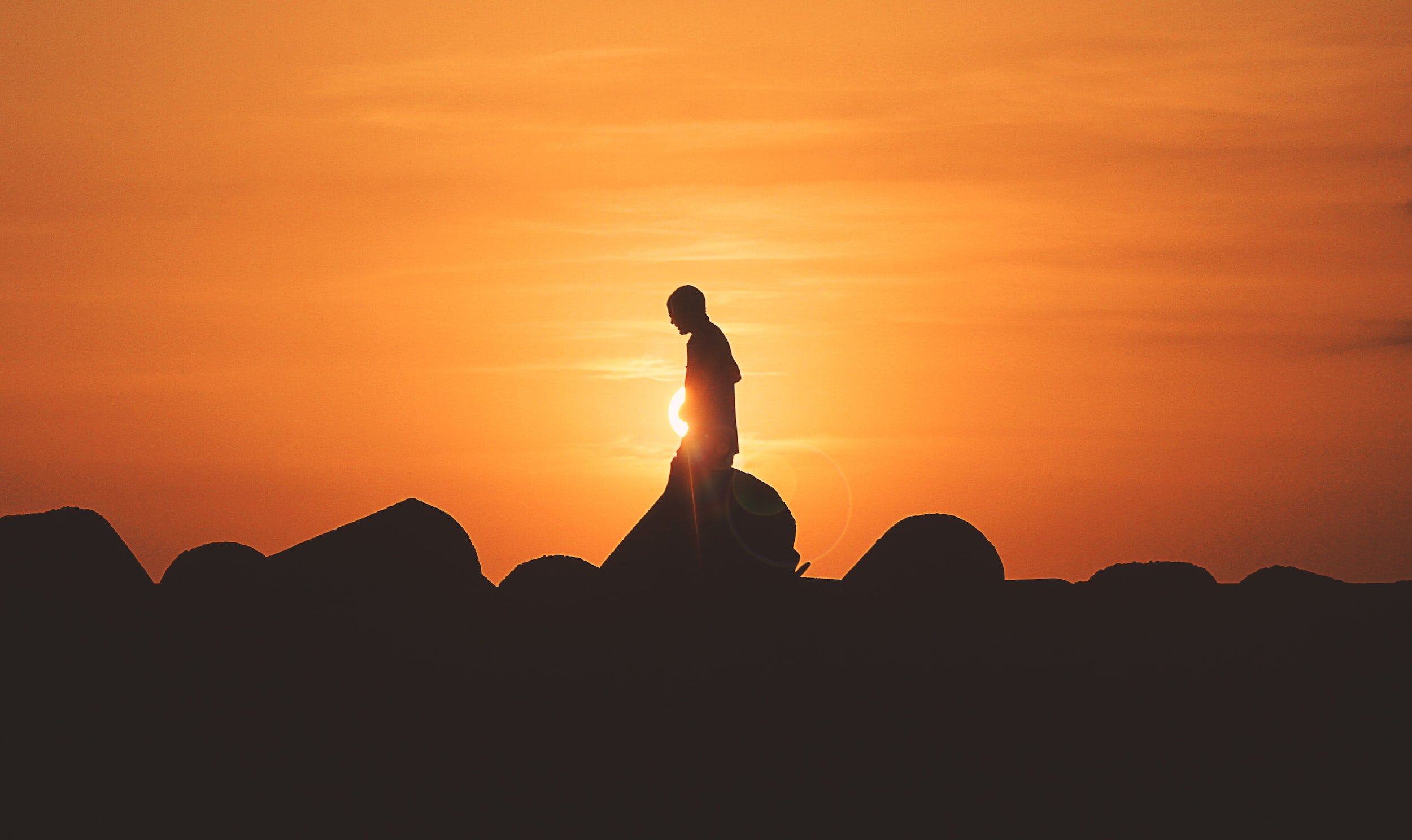 Silhouette of a person standing on rocks during sunset.